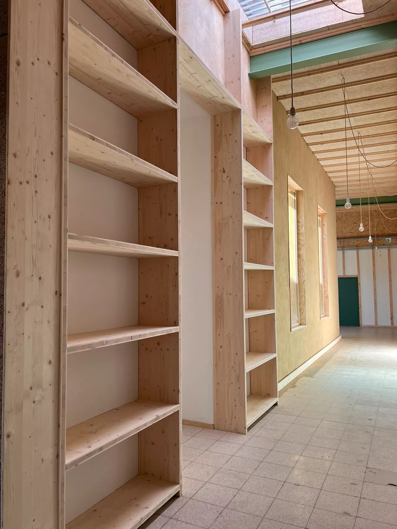 Aménagement intérieur du bâtiment démonstrateur de Noeux-environnement, avec des étagères sur mesure en bois massif et des murs enduits de terre crue, illustrant l’intégration de matériaux biosourcés et la qualité architecturale du projet.